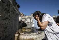 Una turista si rinfresca da una fontana pubblica a Roma..