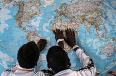 Minori eritrei in centri accoglienza guardano una carta geografica mondiale.