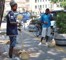 Curvi sotto il sole di una domenica d'agosto, a pulire le erbacce dalle strade, Friday e Celestian, nigeriani di 25 e 28 anni,