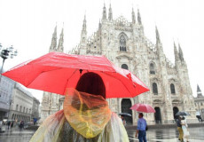 Una turista passeggia sotto la pioggia battente in piazza Duomo a Milano