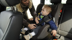 Una madre allaccia la cintura del seggiolino al suo bambino in macchina. (Avvenire)