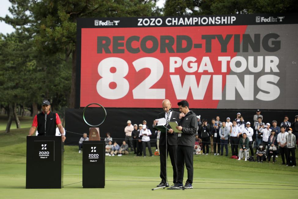 Tiger Woods sul podio in Giappone davanti un cartellone che annuncia il record de 82 vittorie sul PGA Tours. Immagine d'archivio.