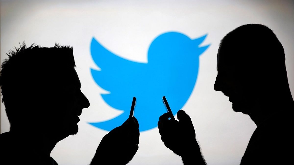 L'ombra di due persone guardando il cellulare e sullo sfondo il logo di Twitter.