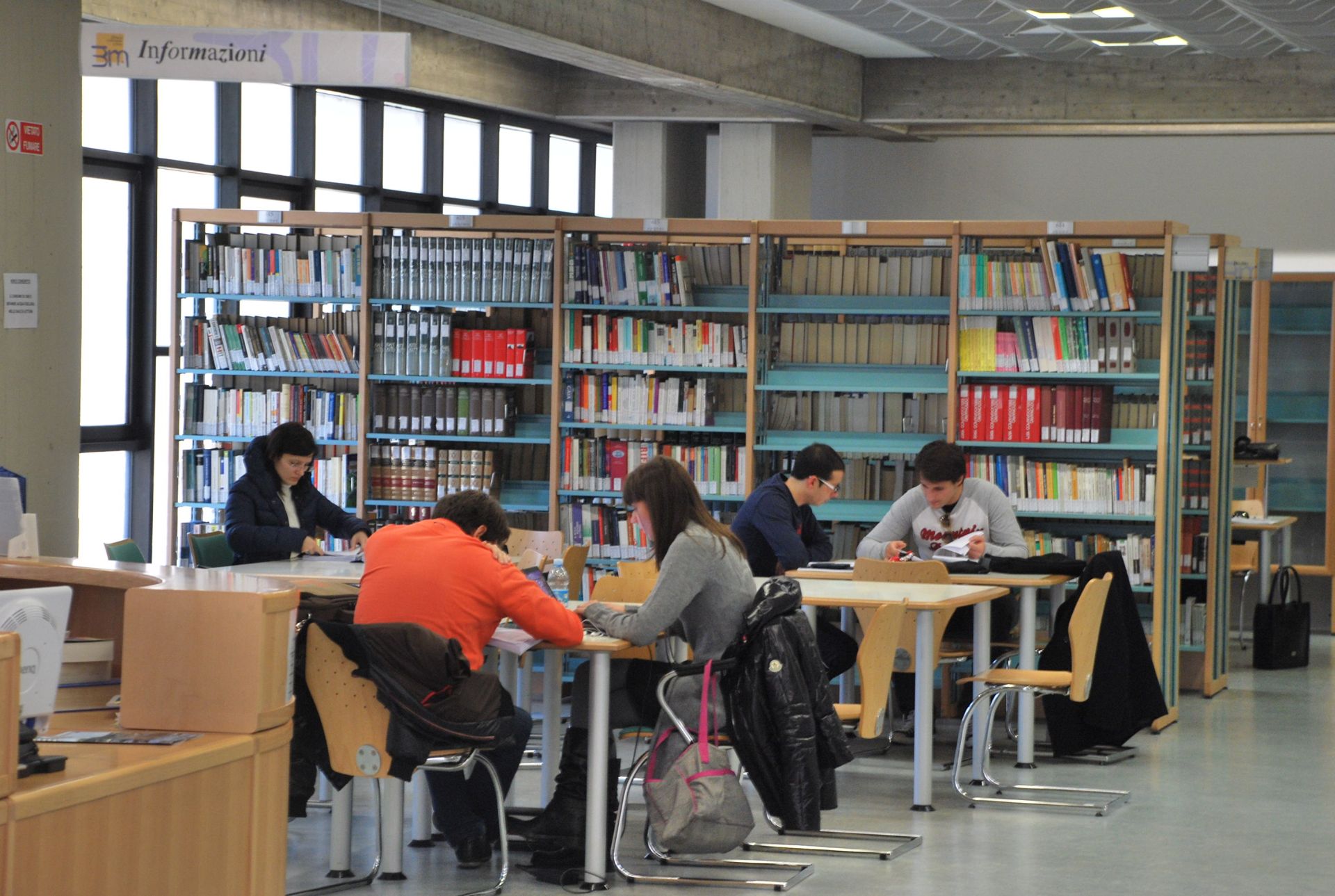 Persone leggono e studiano sui banchi di una biblioteca.