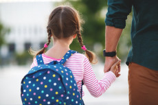Un papà porta a scuola la figlia per mano.