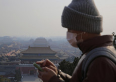 Un giovane porta una mascherina a Pechino. Sullo sfondo la Cittá proibita.