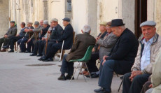 Un gruppo di anziani prende il sole seduti in panchine.