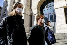 Persone con mascherine per proteggersi dal Coronavirus in piazza affari davanti all'ingresso della Borsa a Milano.