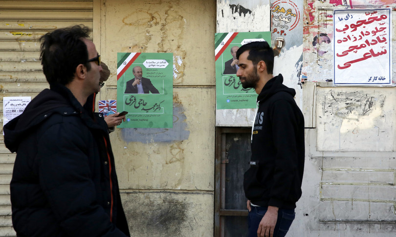 Cittadini passano davanti dei poster elettorali in una strada di Teheran. (money.it)