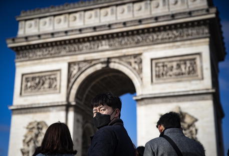 Un turista indossa una mascherina davanto all'Arco di Trionfo a Parigi.