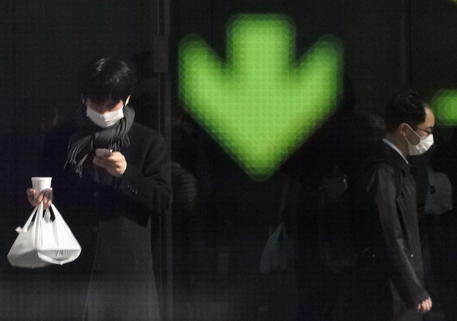 Cittadini con mascherine passano di fronte a un schermo tabellone del mercato bursatile a Tokyo, Giappone.
