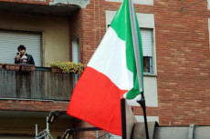 Una persona in balcone e la bandiera italiana in primo piano.