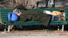 Un clochard addormentato su una panchina di un parco del centro di Milano.