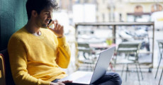 Un giovane parla per telefono mentre usa il pc.