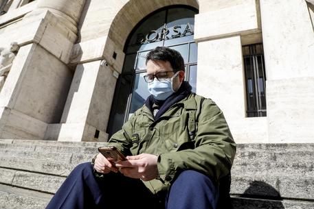 Persona con mascherina per proteggersi dal Coronavirus in piazza affari davanti all'ingresso della Borsa a Milano.