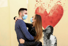 Una coppia di fidanzati con mascherina anti contagio si abbraccia davanti ad un murales