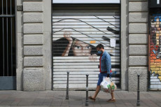 Un pedone davanti ad un negozio con la serranda abbassata a Milano.