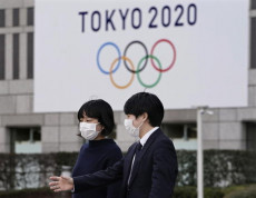 Due passanti con mascherine camminando davanti un cartello in una stazione della metropolitana di Tokyo sulle Olimpiadi Tokyo 2020.