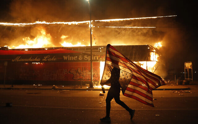Un manifestante passa con la bandiera statunitense davanti ad un negozio in fiamme in Minneapolis, durante le proteste per l'uccisione dell'afroamericano George Floyd,