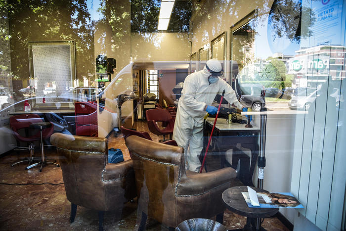 Operatori in tuta bianca sanificano un negozio per parrucchiere in vista della riapertura