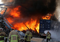 Una squadra di pompieri cercano di soffocare le alte colonne di fiamme s'innalzano nel porto di Beirut.