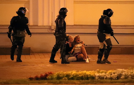 Due donne piangono sedute a terra circondate da agenti della polizia bielorussa.