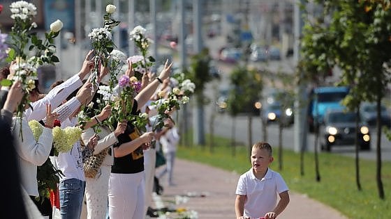 Donne, vestite di bianco, coi fiori in mano, manifestano in una stradadi Minsk.