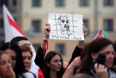 Bielorussia, una manifestante con un cartello con la faccia di Lukashenko dietro le sbarre.