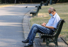 Uomo con la mascherina seduto in panchina durante un passeggiata nel parco