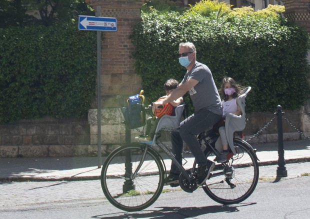 Un papà in bici con i suoi bimbi indossando la mascherina.