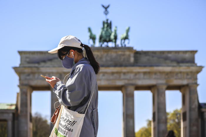 Una persona con la mascherina di fronte alla Porta di Brandenburgo a Berlino.