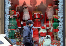 Un uomo con la mascherina di fronte alla vetrina di un negozio con addobbi di Natale.