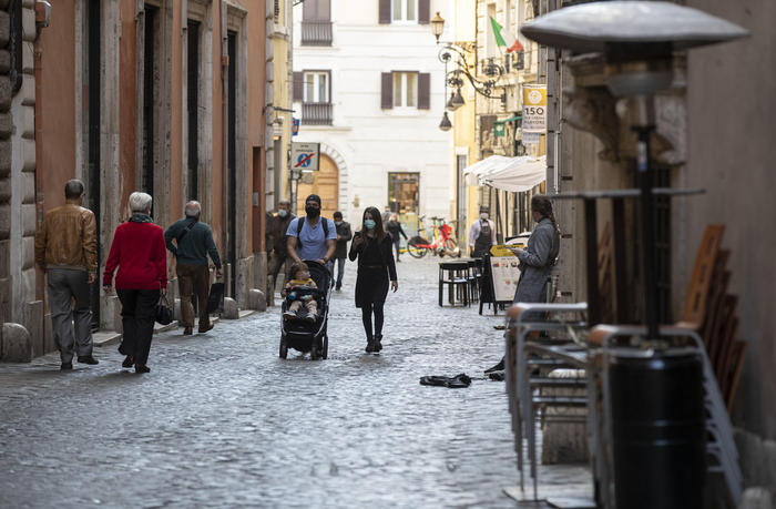 Persone con mascherine passeggiano in una strada di Roma