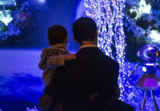 Un uomo con un bimbo in braccio osserva le luci di Natale.