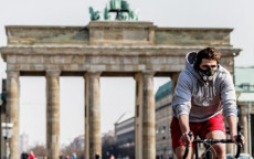 Ciclista con mascherina pedala di fronte alla Porta di Brandeburgo a Berlino.
