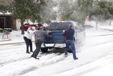 Residenti di Round Rock spingono una pickup che slitta sulla strada dopo una tormenta di neve in Texas.