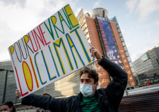 Attivista per il clima manifesta davanti alle istituzioni europee, con un cartello con la scritta "Per una vera legge sul clima" (ANSA/EPA)