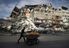 Un uomo spinge una carriola davanti un edificio semidistrutto dai bombardamenti a Gaza. (