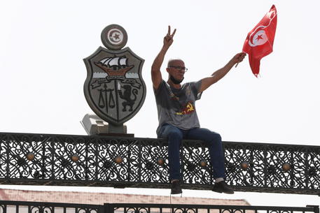 Un manifestante siede sulla cima del cancello del parlamento in Tunisia.