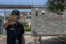 Un agente della polizia cinese fa segni ad un fotografo di non scattare foto davanbti all'ambasciata del Canada a Pechino