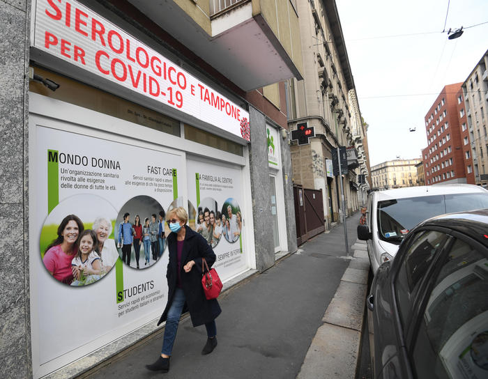 Una donna con il volto coperto da una mascherina sanitaria cammina accanto a una farmacia in Blignyvia adiacente all' Università Bocconi, Milano, 9 marzo 2021.