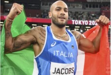 Marcell Jacobs con la bandiera italiana sulle spalle.