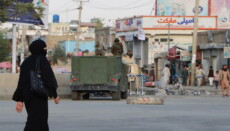 Una donna donna passa di fronte ad un mezzo corazzato dei talibani nei pressi dell'aeroporto di Kabul.