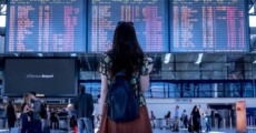 Giovane emigrante guarda tebellone delle partenze.