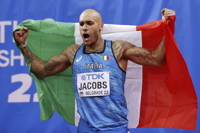 Lamont Marcell Jacobs festeggia l'oro nei mondiali indoor avvolto dalla bandiera italiana.