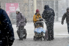 Adulti e bambini ucraini attraversano il confine tra l'Ucraina e la Moldova sotto una forte nevicata.