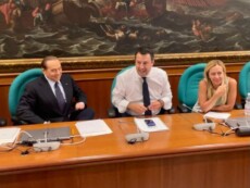 Silvio Berlusconi, Matteo Salvini e Giorgia Meloni seduti accanto e sorridenti sotto la mega tela della Battaglia di Lepanto che campeggia nella sala Salvadori di Montecitorio, 27 luglio 2022.