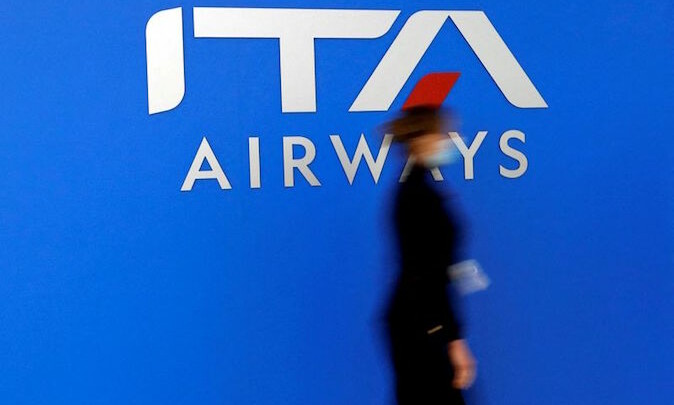 Una donna cammina davanti al tabellone con il logo di Ita