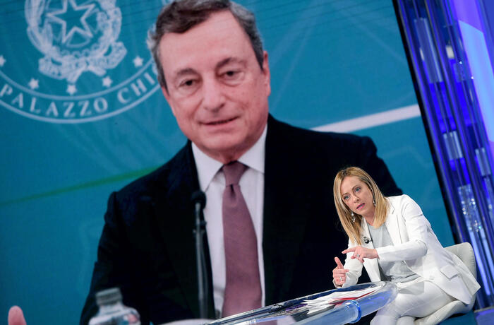 Giorgia Meloni, durante il programma Porta a Porta con la foto di Mario Draghi sul fondo.