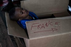 Un bambino migrante in uno scatolone con la scritta "France"